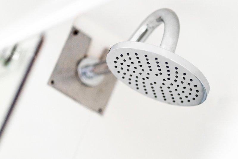 Modern bathroom shower head mounted on white tiled wall with valve