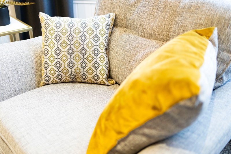 Beige upholstered sofa with patterned and yellow cushions, bright interior lighting
