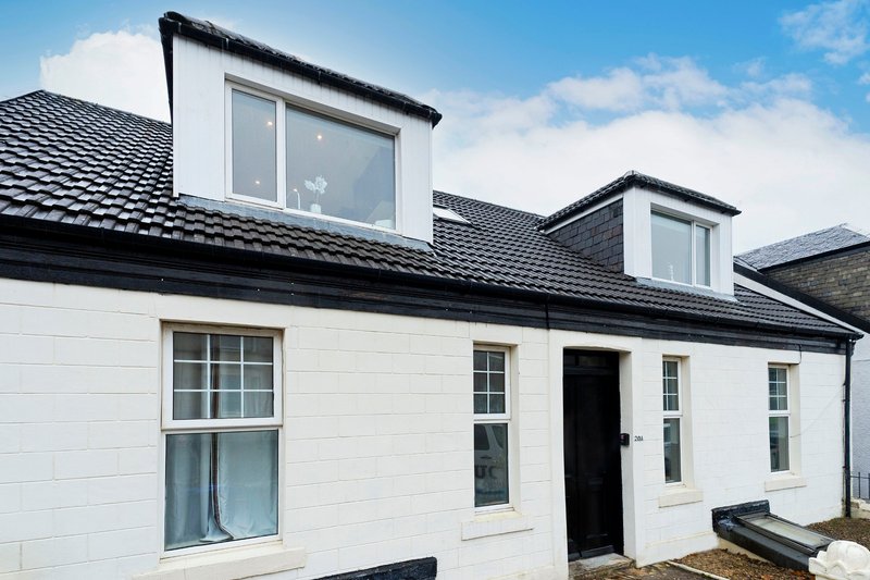 White rendered house with black roof, dormer windows and dark front door