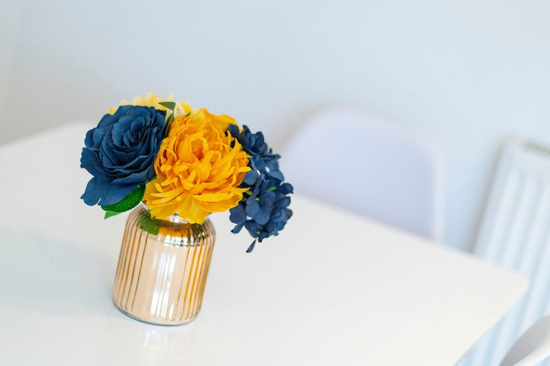 White table with blue and yellow flower arrangement in striped glass vase
