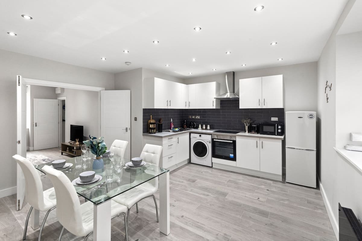 Modern open-plan kitchen and dining area with white cabinetry, stainless steel appliances, and glass dining table
