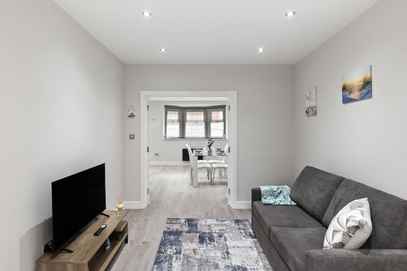 Modern living room with gray sofa, TV stand, wooden flooring and open doorway to bedroom