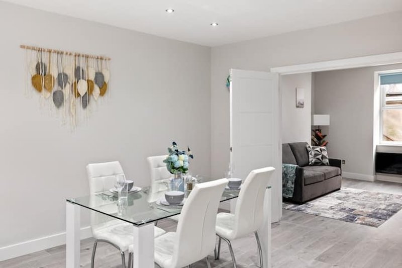 Modern open-plan living and dining area with glass table, white chairs, and hanging brass decor