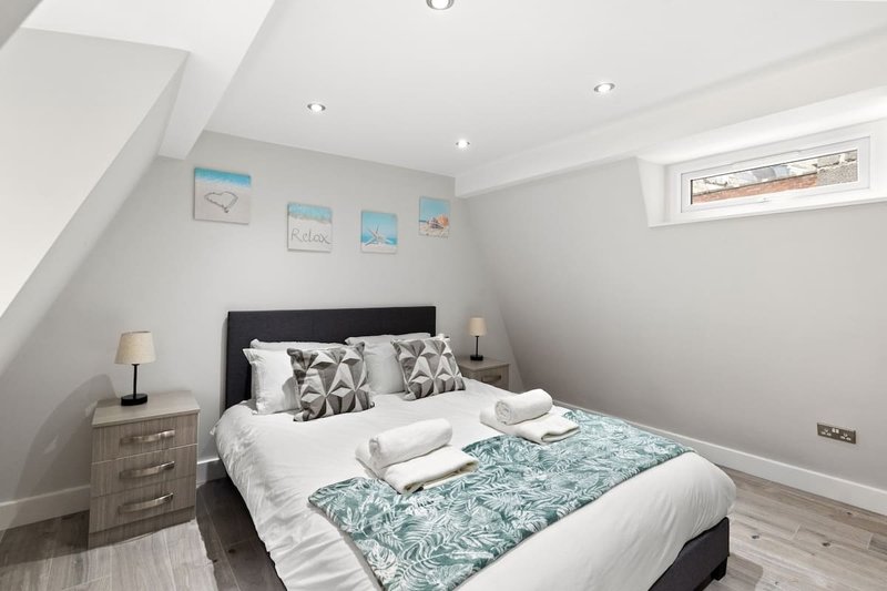 Attic bedroom with double bed, patterned cushions, wooden bedside table and small framed wall art