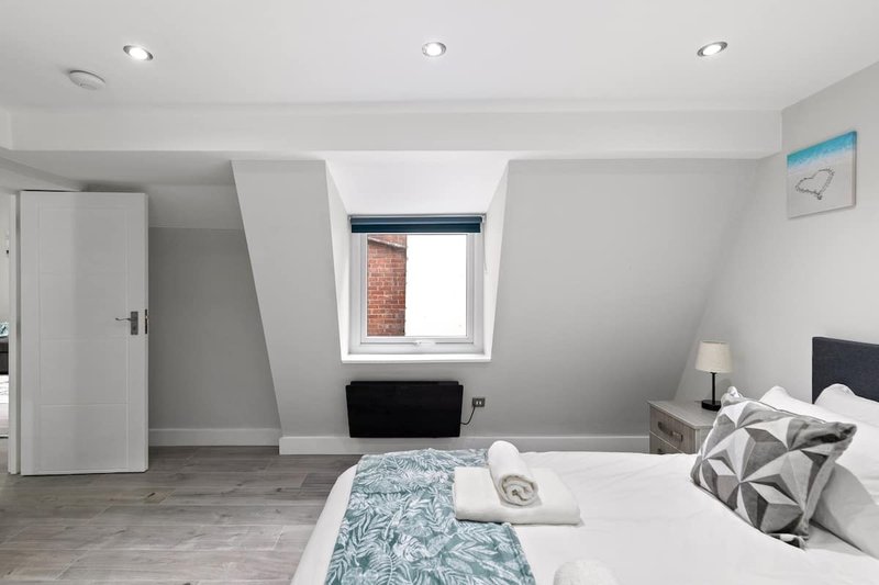 Modern bedroom with double bed, geometric cushions, skylight window and wooden flooring