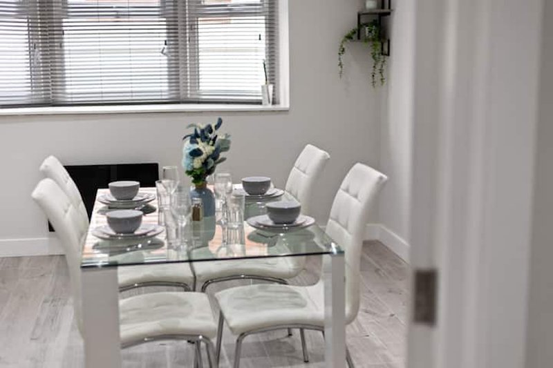 Modern dining room with glass table, white quilted chairs and place settings