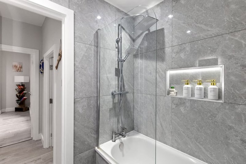 Modern bathroom with walk-in shower, grey tile walls, built-in shelf and recessed lighting