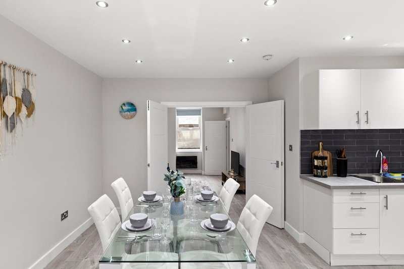 Modern open-plan kitchen and dining area with white cabinetry, glass dining table, and black splashback