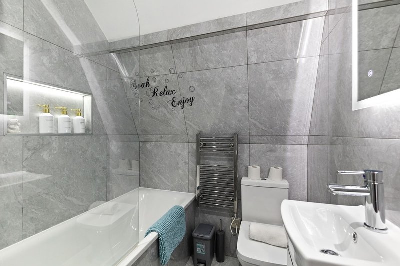 Modern bathroom with grey tile walls, white bathtub, sink, and glass shower enclosure