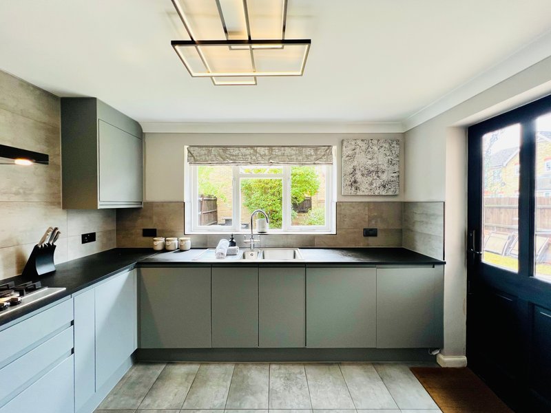 Modern kitchen with white and grey cabinetry, black countertop, and large window overlooking garden