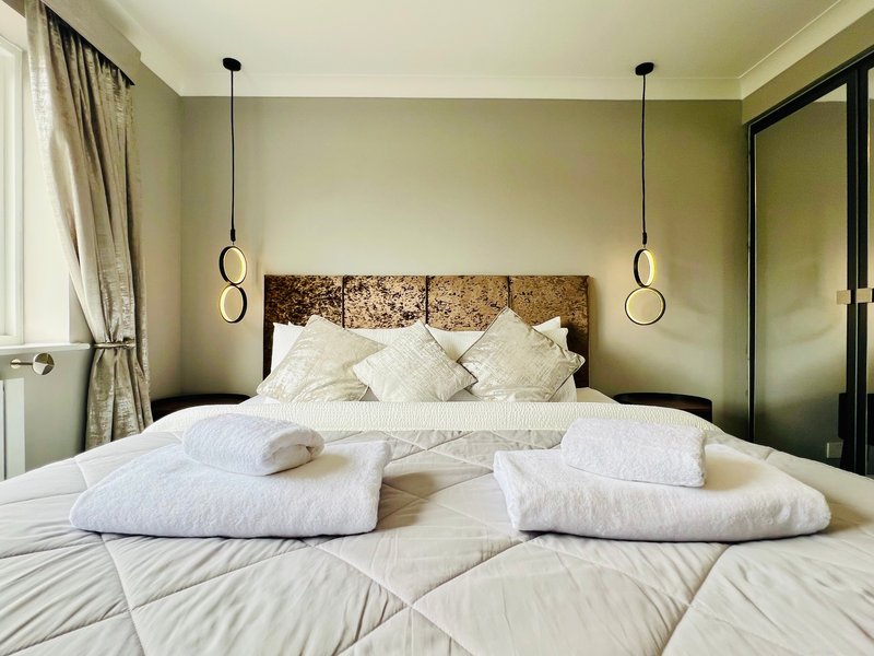 Modern bedroom with double bed, white pillows, pendant lights, and sage green walls