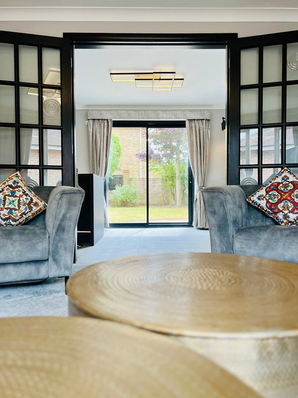 Modern living room with blue armchairs, round wooden table, black-framed doors and garden view