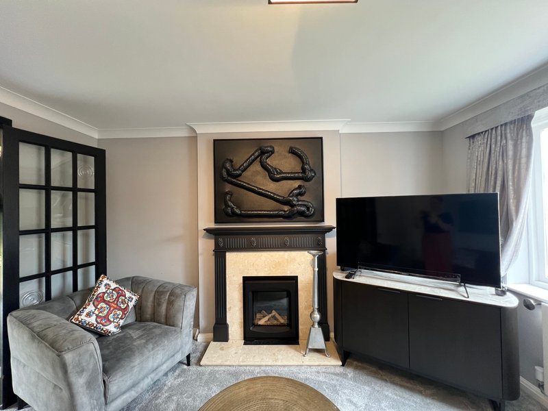 Modern living room with gray armchair, fireplace, wall-mounted TV, and large windows