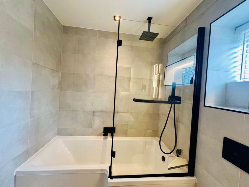 Modern bathroom with walk-in shower, glass enclosure, black fixtures and cream tile walls