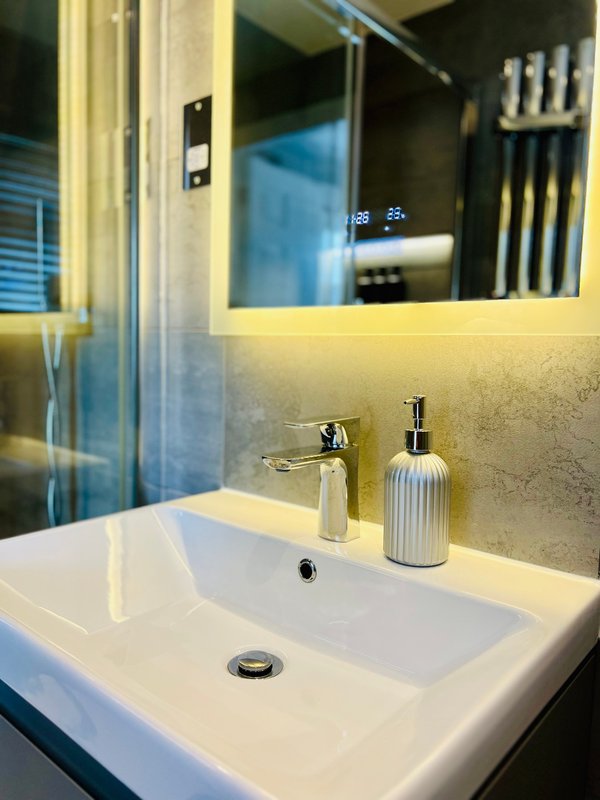 Modern bathroom sink with chrome faucet, soap dispenser, and illuminated mirror