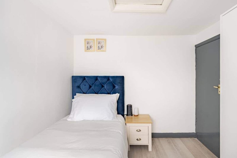 Compact bedroom with single bed, blue quilted headboard, wooden nightstand, and skylight
