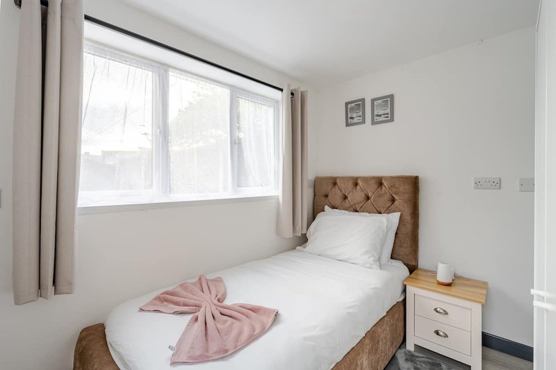 Bedroom with single bed, pink throw, wooden headboard, bedside table and window