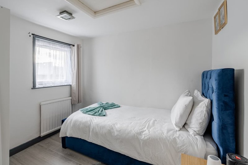 Bright bedroom with double bed, blue headboard, white bedding and window with curtains