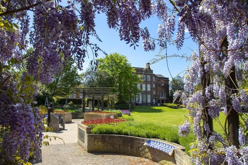 Large brick house with manicured garden, wisteria-framed view, lawn and flower beds