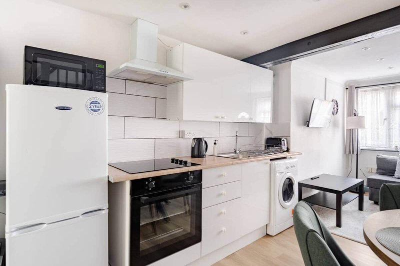Modern kitchen with white cabinetry, integrated oven, white fridge, washing machine and wooden countertops