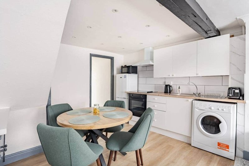 Modern open-plan kitchen-diner with white cabinetry, dining table, green chairs and washing machine