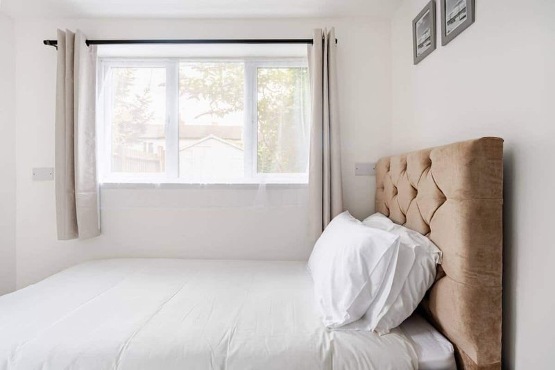 Bright bedroom with single bed, upholstered headboard, white bedding and window with garden view