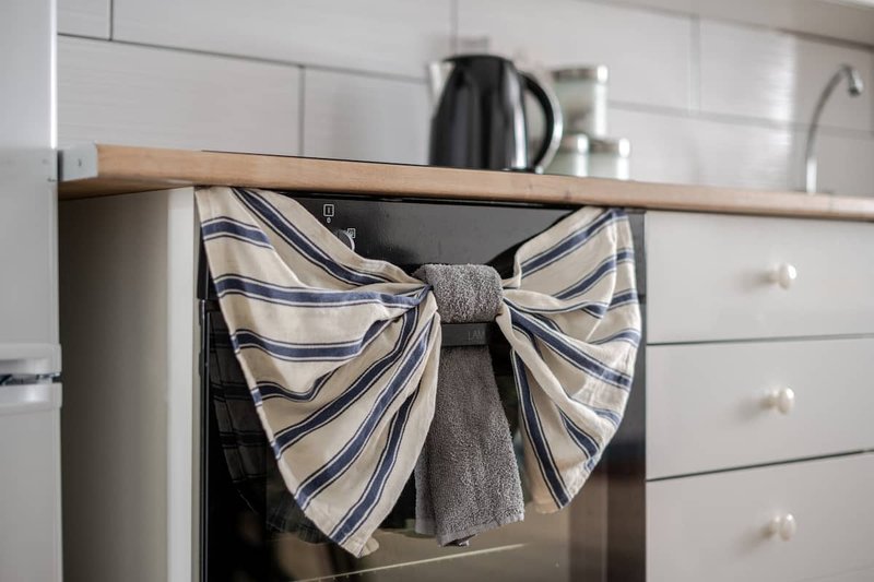Modern kitchen with white cabinetry, wooden shelf, and striped kitchen towel