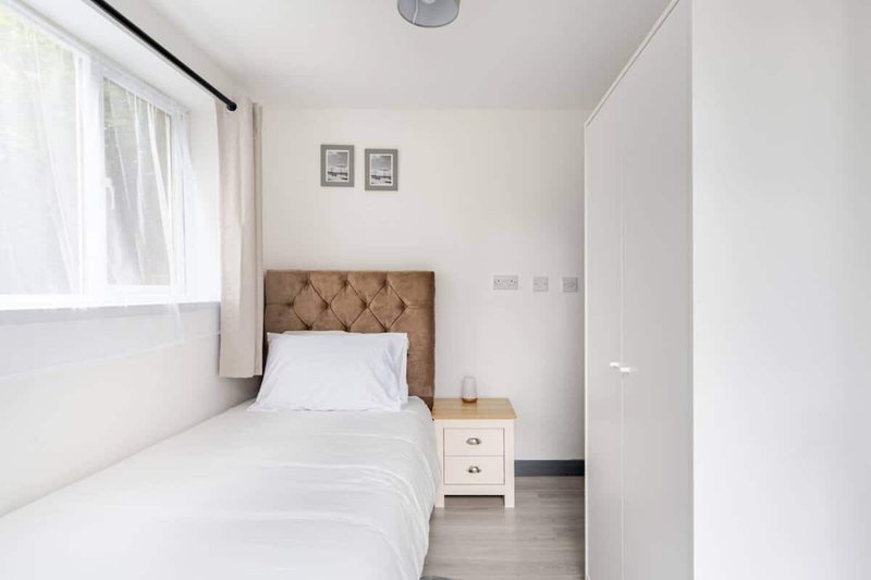Single bedroom with upholstered headboard, white bedding, nightstand and window