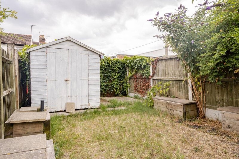 Residential garden with white shed, wooden fencing, overgrown grass and climbing ivy