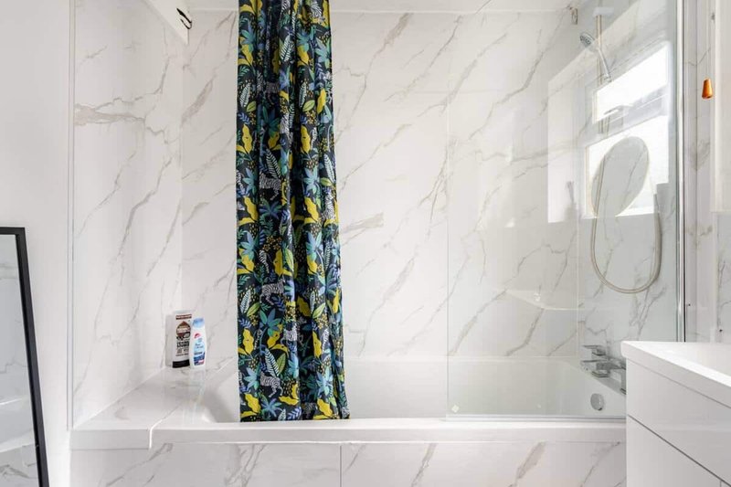 Modern bathroom with marble-effect tiles, white bathtub, glass shower screen and patterned shower curtain