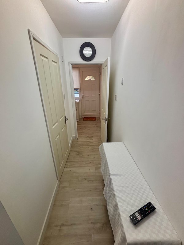 Narrow hallway with wooden flooring, white doors, wall clock, and mattress