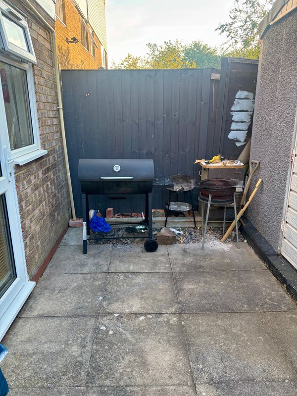 Enclosed outdoor patio area with barbecue grill, seating furniture, and storage against dark fence