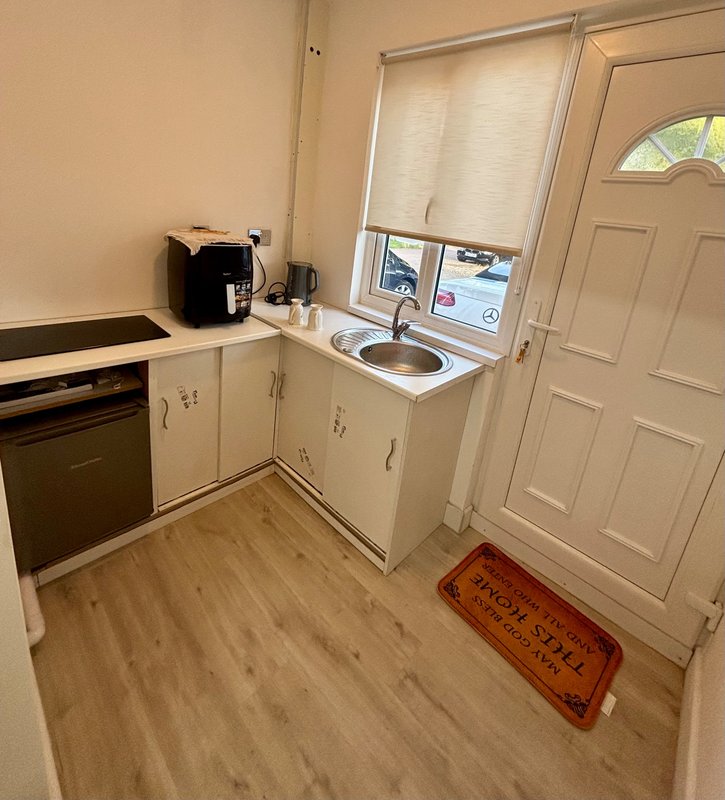 Compact kitchen with cream cabinets, black oven, sink, and wooden floor
