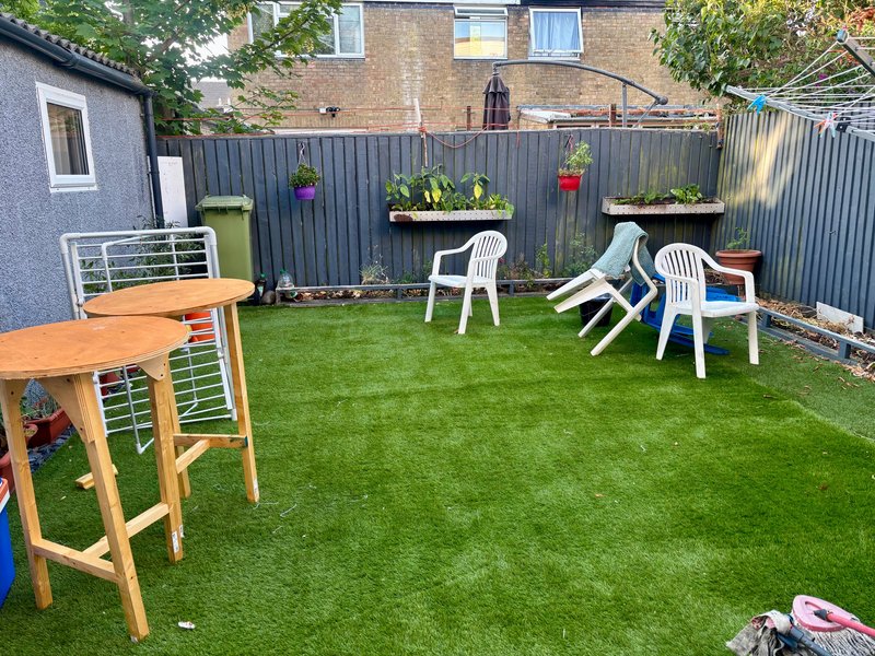 Enclosed backyard garden with artificial grass, wooden table, white chairs and planted containers