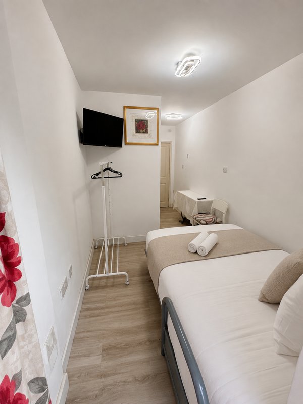 Narrow bedroom with two single beds, wall-mounted TV, wooden flooring and white walls