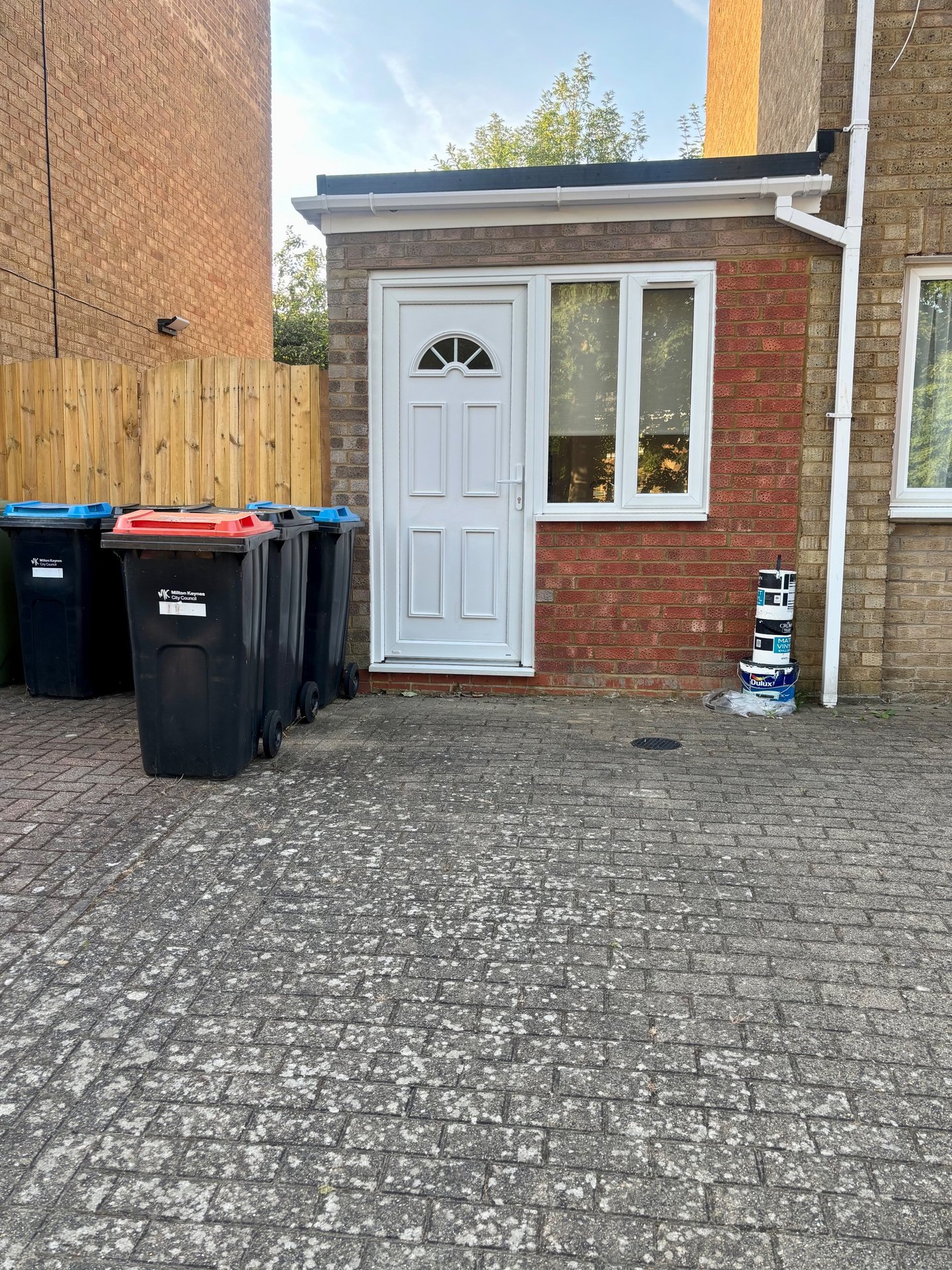 Brick property entrance with white door, driveway, and colourful waste bins
