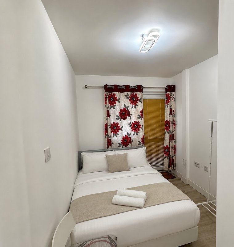 Small bedroom with double bed, red floral curtains, white bedding and neutral décor