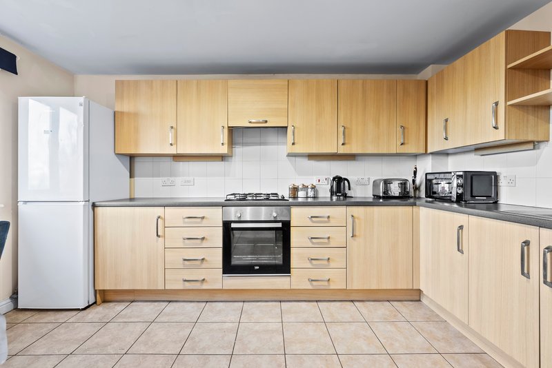 Modern kitchen with light wood cabinetry, white appliances, gas stove and tiled floor.