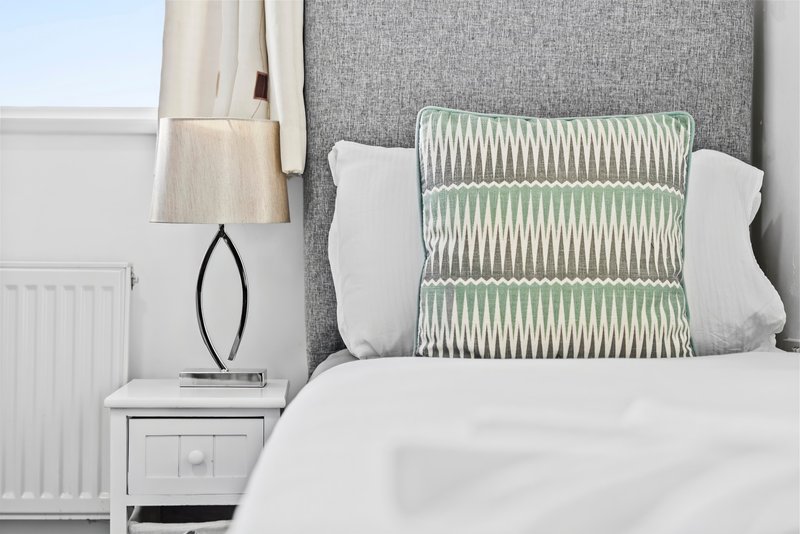 Modern bedroom with white bedding, green patterned cushion, grey headboard and white nightstand