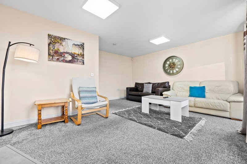 Modern living room with cream sofa, wooden armchair, white coffee table and wall clock