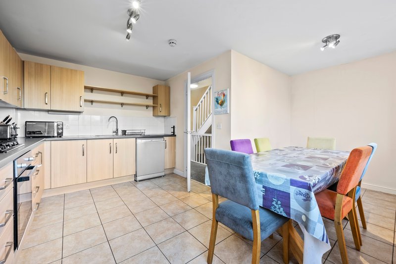 Open-plan kitchen and dining area with wooden cabinets, dining table and colorful chairs