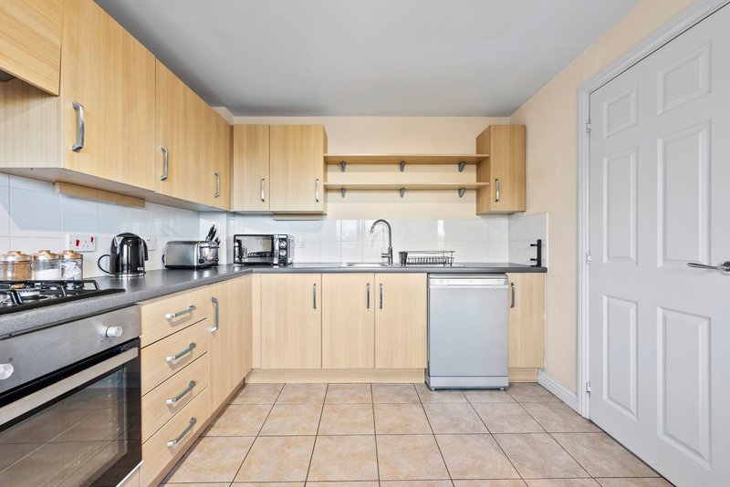 Modern kitchen with light wood cabinets, stainless steel appliances, and tiled flooring
