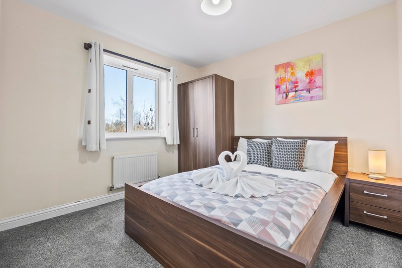 Bright bedroom with double bed, wooden furniture, window with white curtains, colorful artwork.