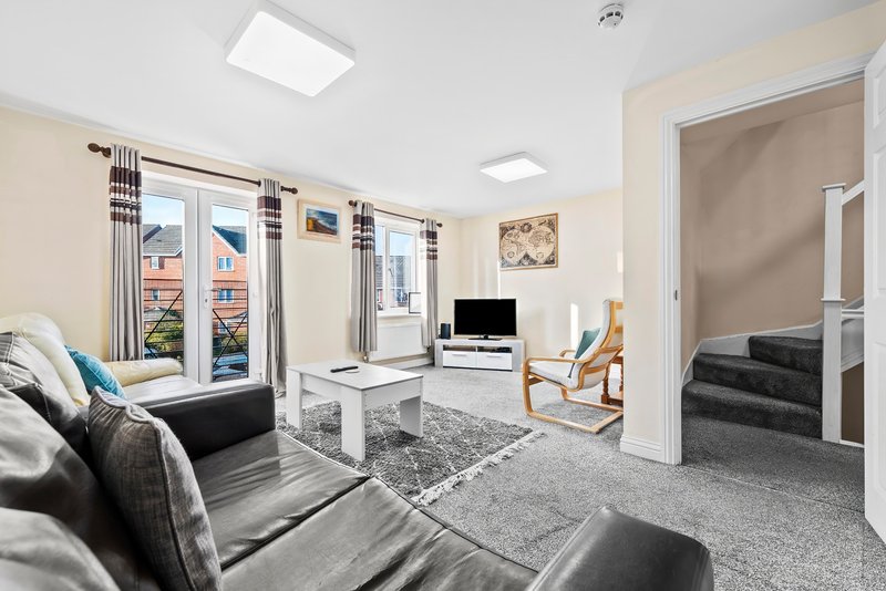 Open-plan living room with sofas, TV, wooden chair, large windows and staircase entrance