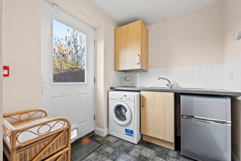 Compact kitchen with washing machine, refrigerator, sink and wooden chair by door