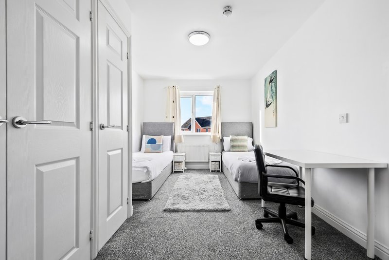 Bright bedroom with two beds, desk, chair, and window with natural light