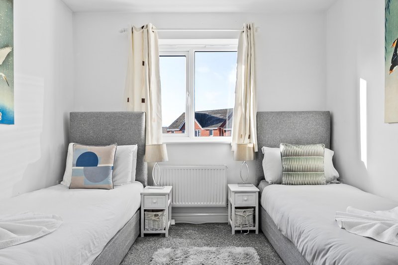 Bright twin bedroom with two beds, grey headboards, window with countryside view