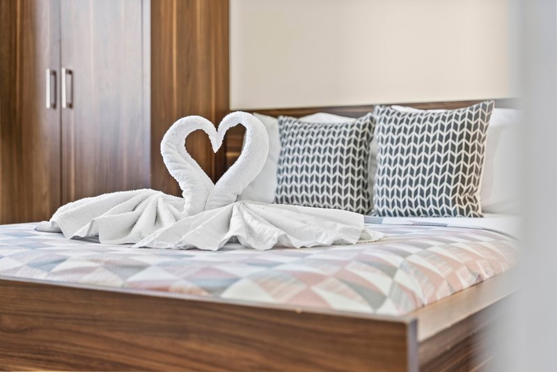 Bedroom with wooden bed frame, heart-shaped towel decoration, patterned pillows and curtains
