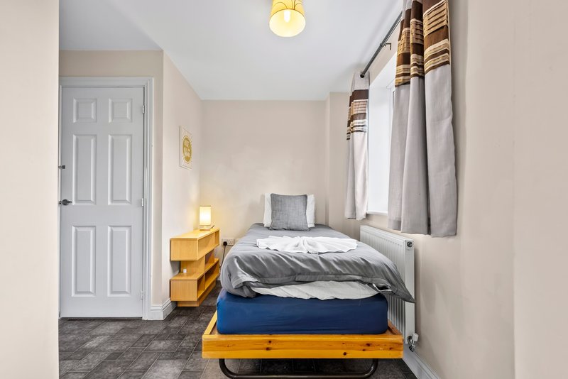 Small bedroom with single bed, wooden frame, grey bedding, window with curtains