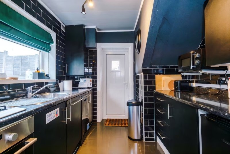 Modern kitchen with black cabinetry, stainless steel appliances including hob, cooker, microwave and a kettle. Also a washing machine.